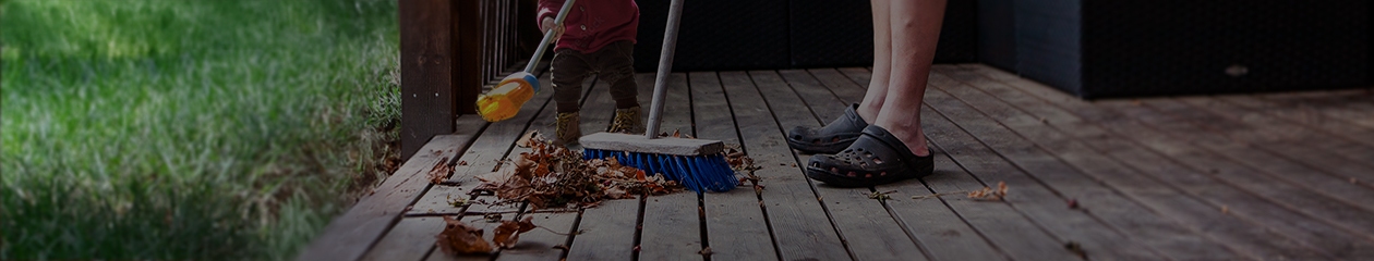 Father and toddler son clean leaves off deck near grassy yard