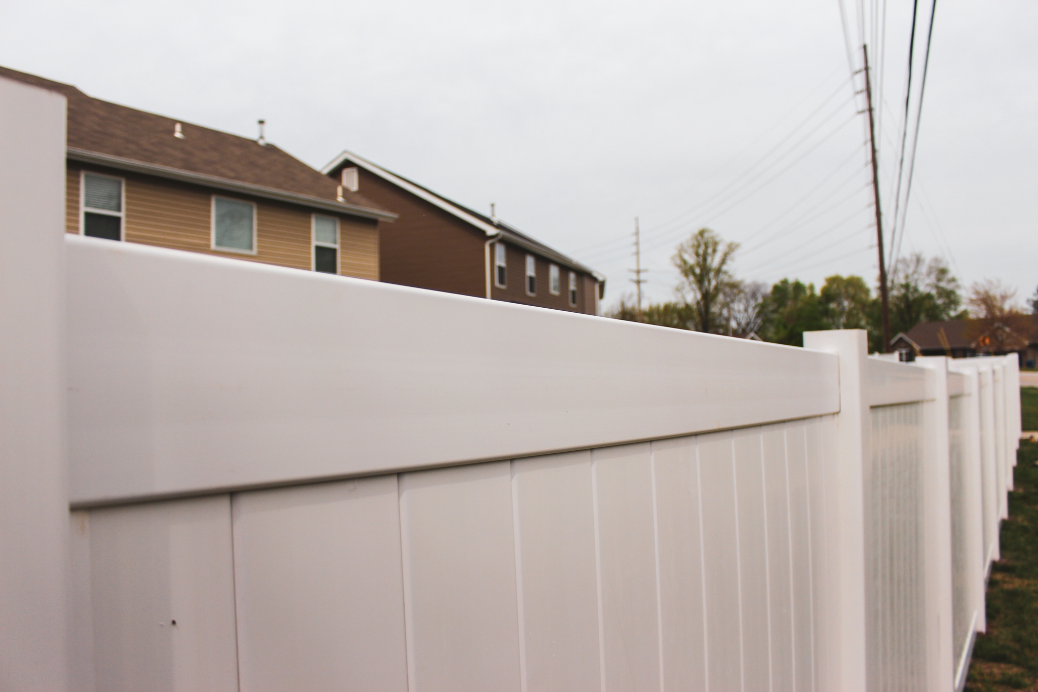 White vinyl privacy fence installed along a residential property line, showcasing professional craftsmanship by Fence Deck and Depot with neighboring homes and utility lines in the background