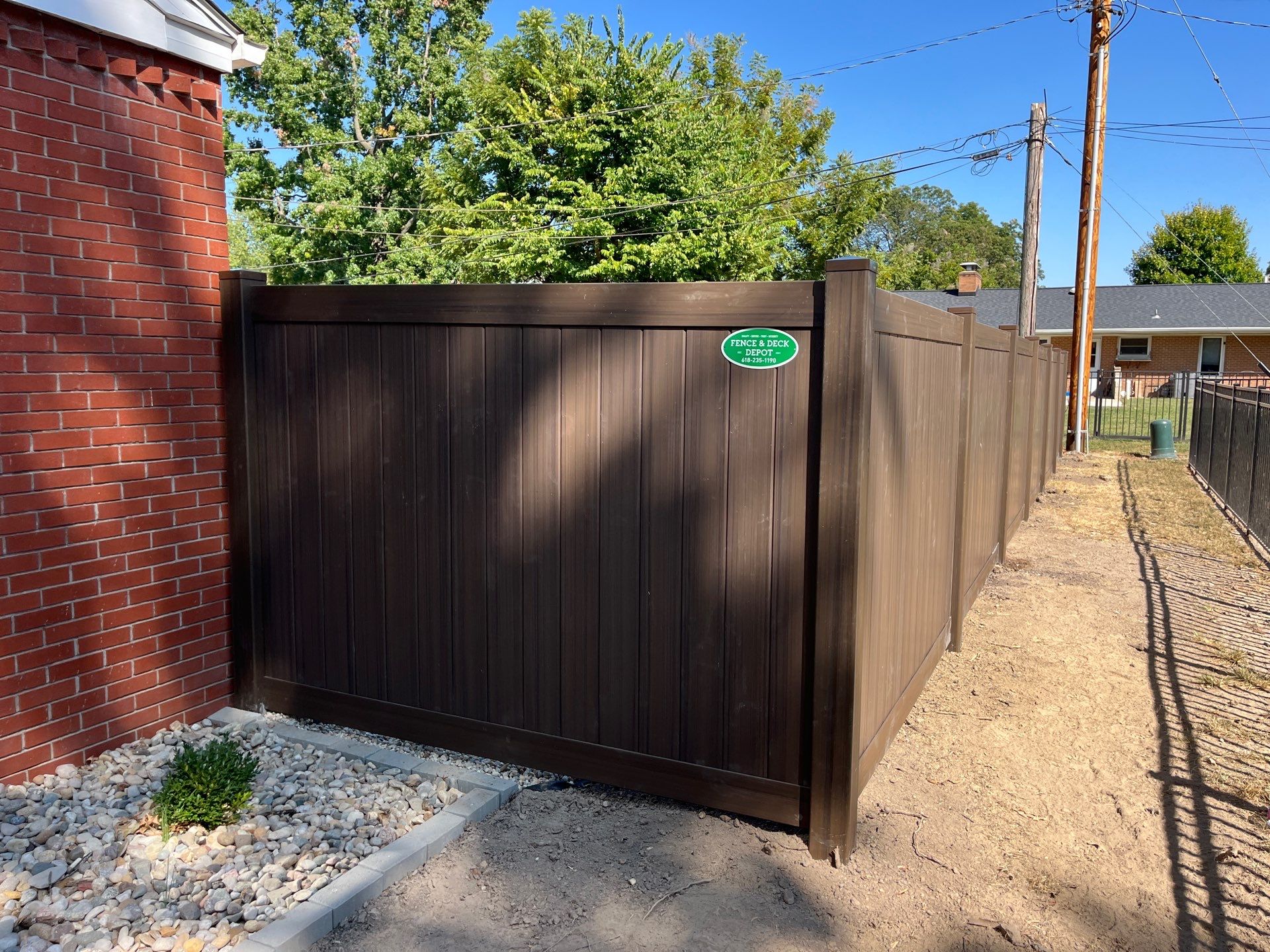 A tall privacy fence that is painted dark brown and features the Fence & Deck Company logo