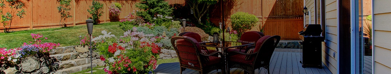 A well landscaped yard with patio furniture, gardens, and a wood fence