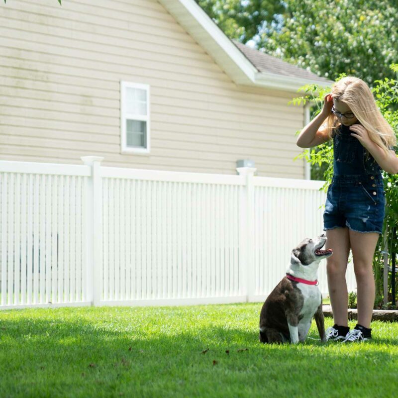 Girl and her dog play in fenced-in yard