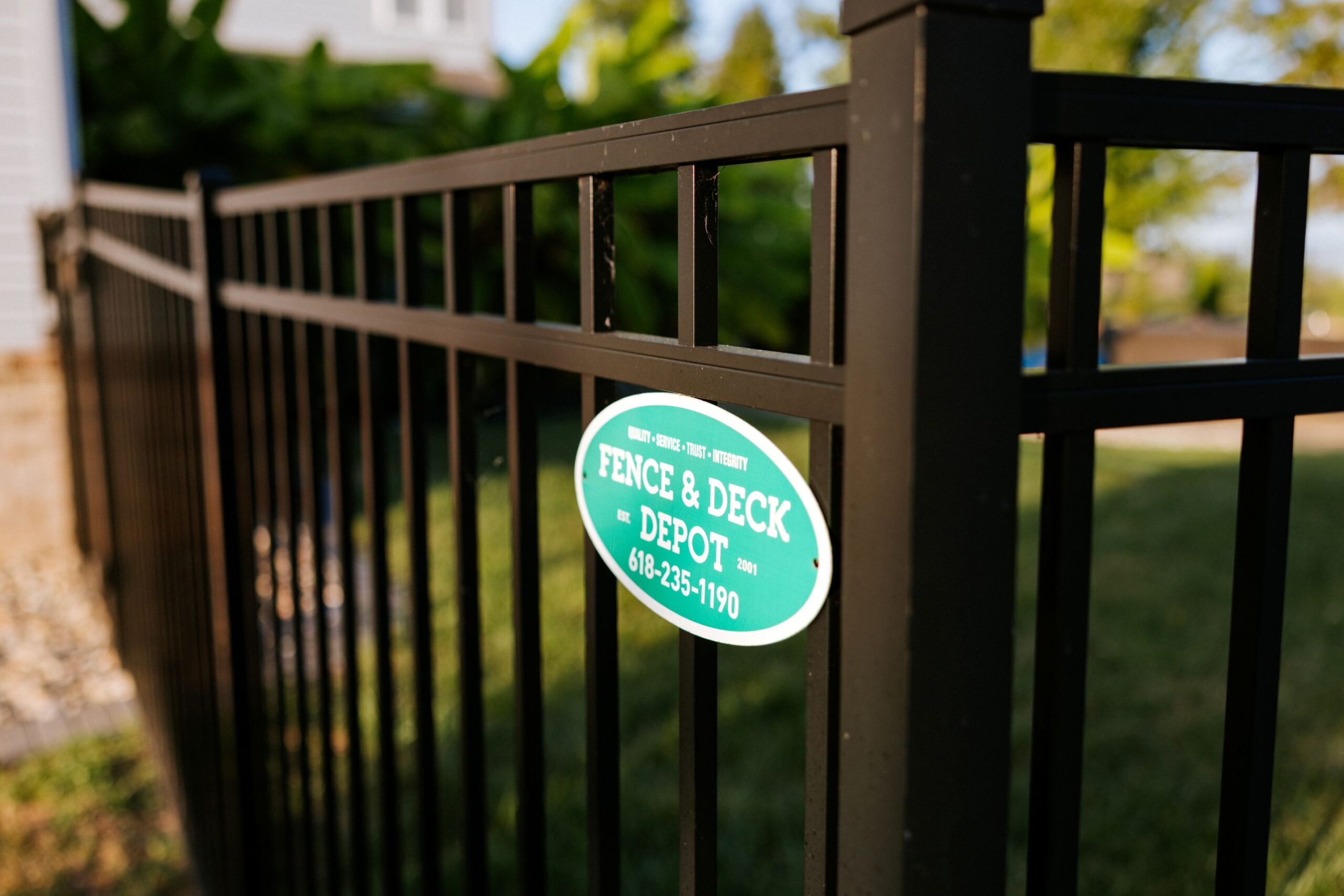 Close-up image of a black aluminum fence with Fence and Deck emblem attached