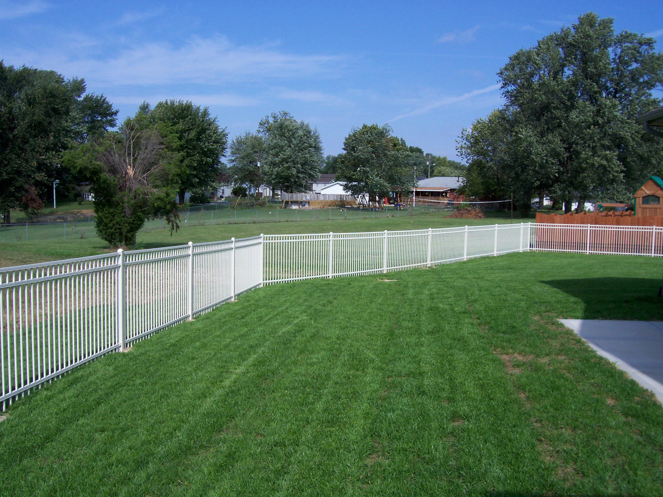 A white aluminum fence surrounds a grassy suburban yard.