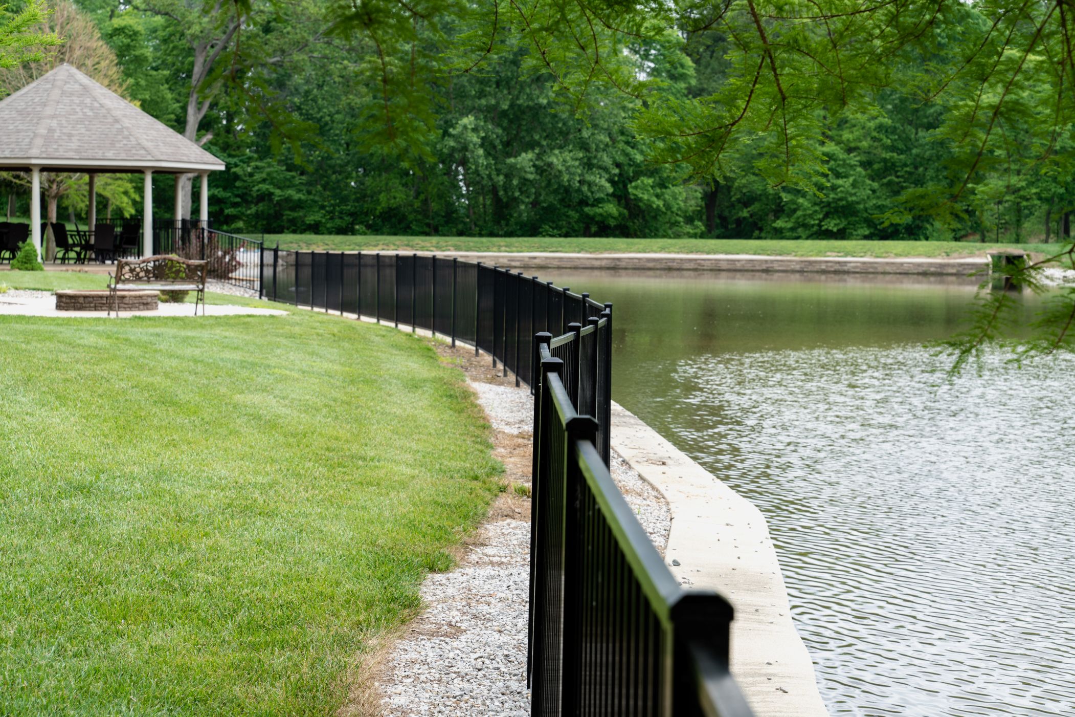 A black aluminum fence separates a residential yard and a large pond.