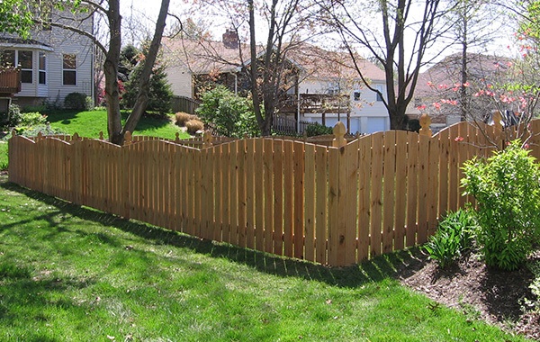 A wide angle image of a scalloped wood privacy fence around a sunny suburban yard
