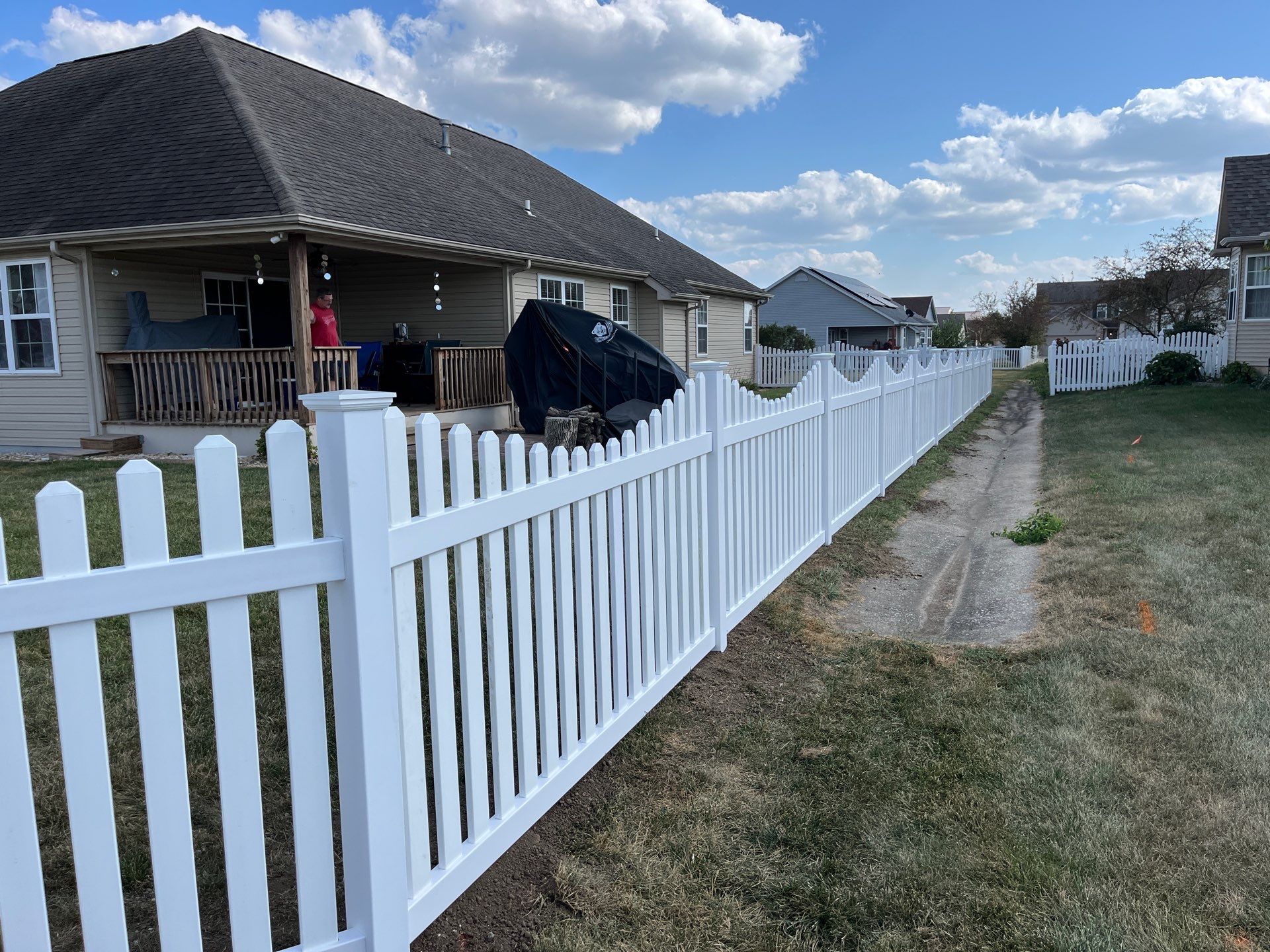 A scalloped white vinyl fence runs along a residential property.