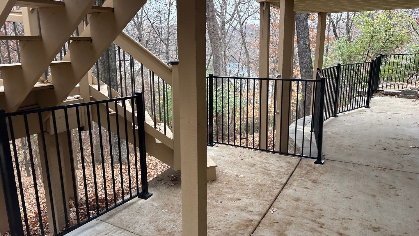 An aluminum fence runs along a patio area underneath a deck