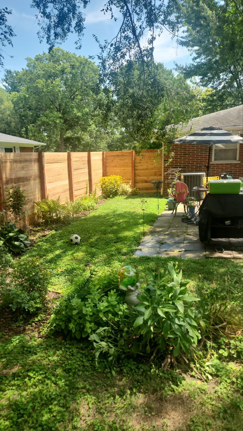 A wood privacy fence with horizontal boards encloses a small backyard with gardens and a patio