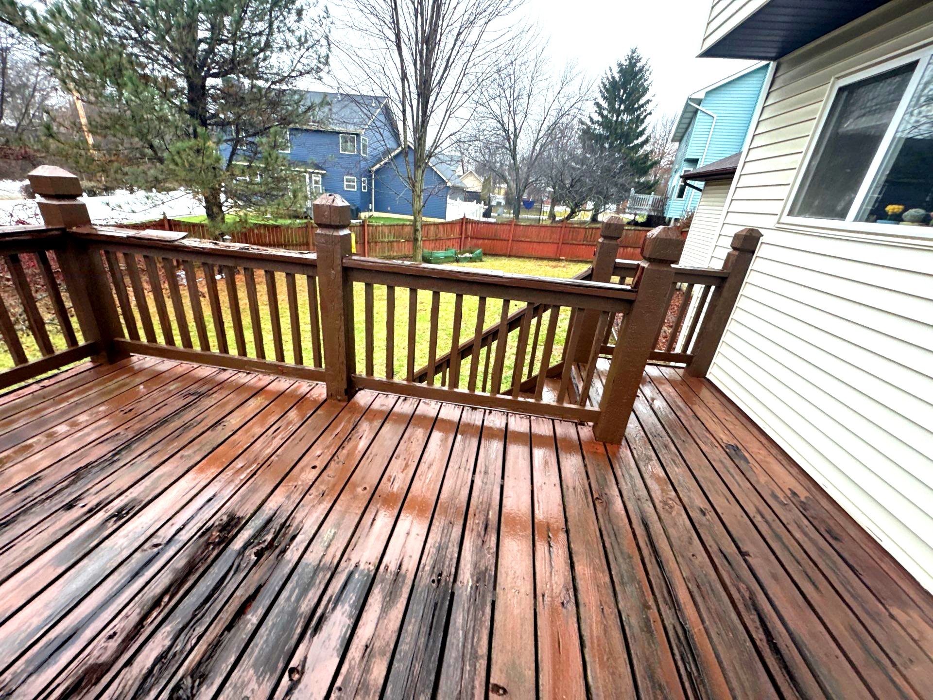 A wood deck overlooks a green backyard on a rainy day
