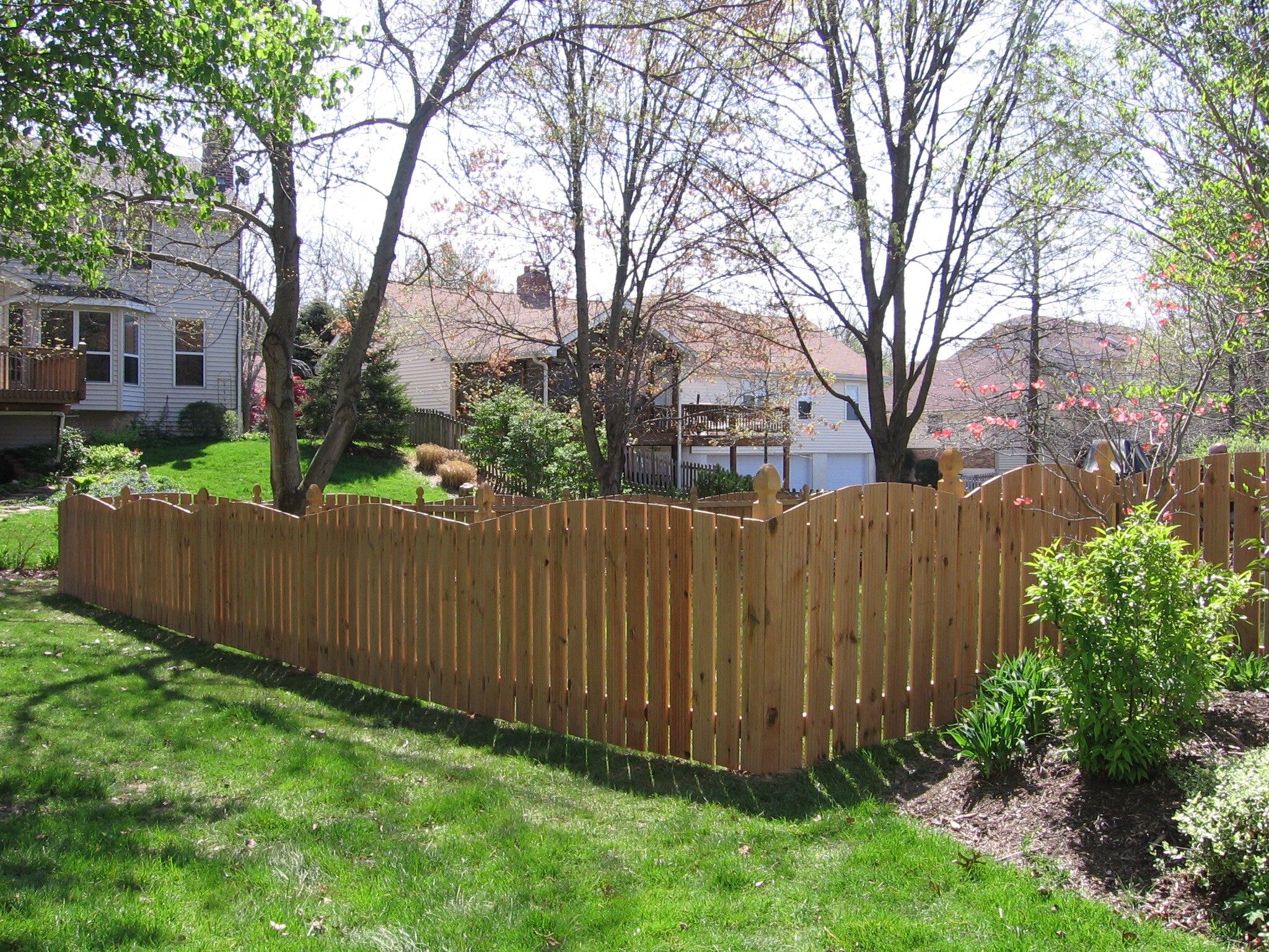 Large scalloped wood fence around a lush green yard