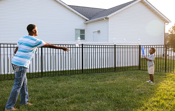A father and sun play catch in their backyard fenced in with an aluminum fence