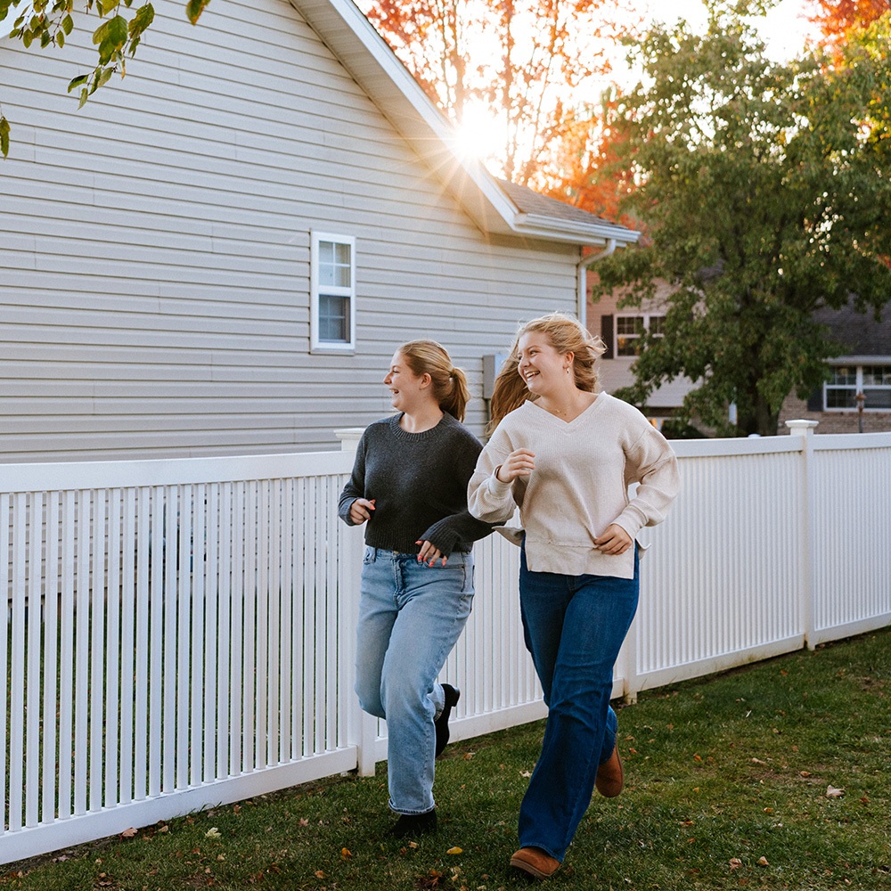 Girls run along a vinyl fence on a sunny evening