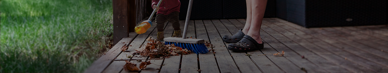 Father and toddler son clean leaves off deck near grassy yard