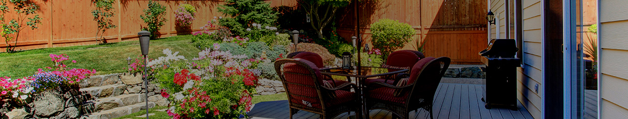 A well landscaped yard with patio furniture, gardens, and a wood fence